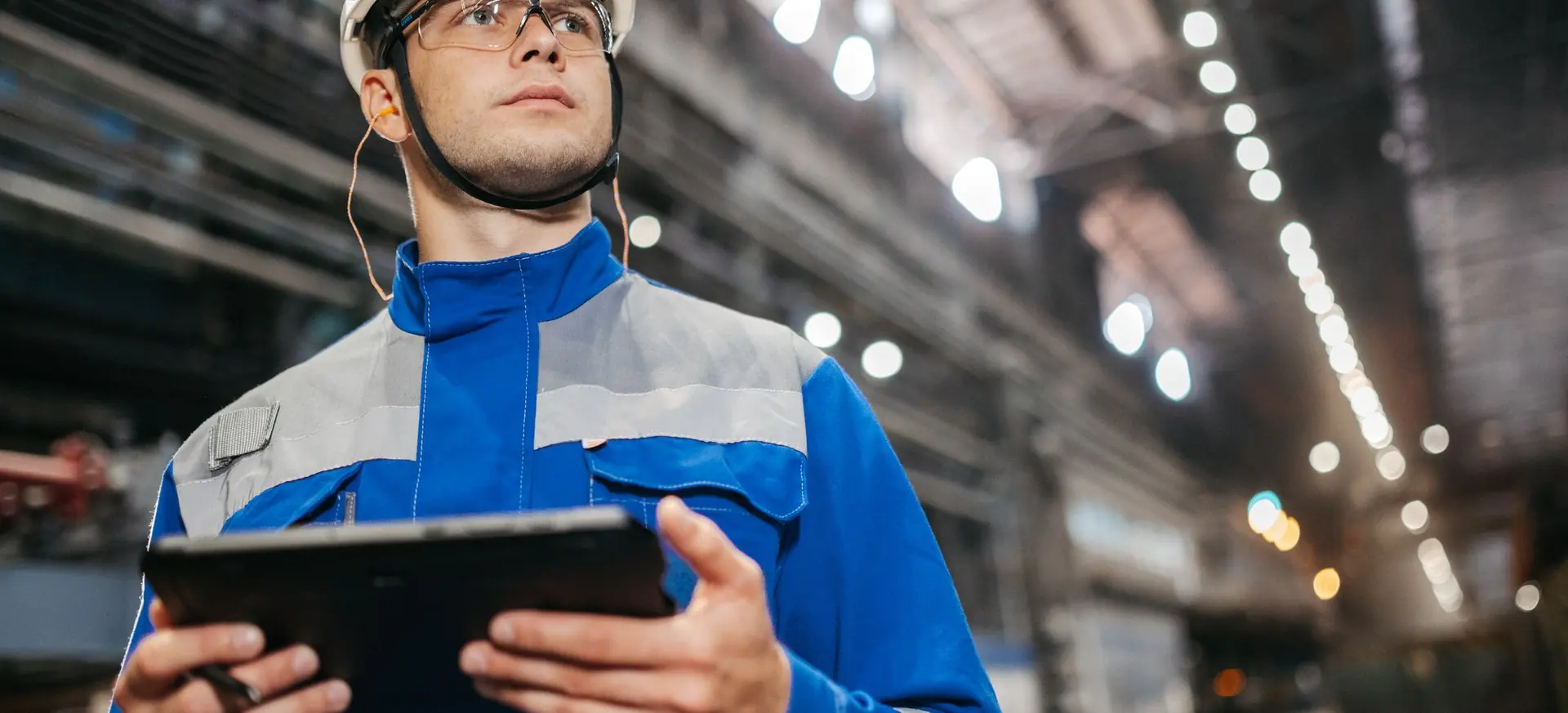 Ouvrier en tenue de sécurité consultant une tablette dans un atelier industriel